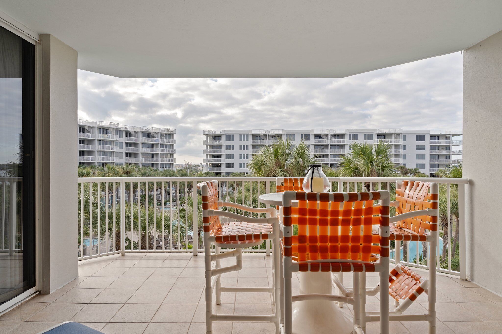 A balcony with a white table and chairs, a view of a residential building, and a tiled floor.