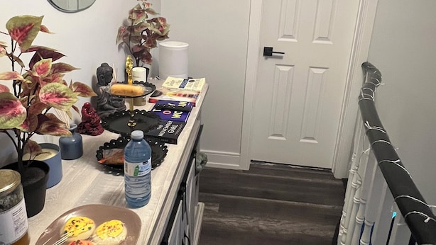 A hallway with a white door labeled "Bathroom" and a counter with various items including a water bottle, books, and decorative objects. - Queen bed Cozy (Brampton)