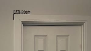 A white door with a sign above it that reads "BATHROOM." - Queen bed Cozy (Brampton)