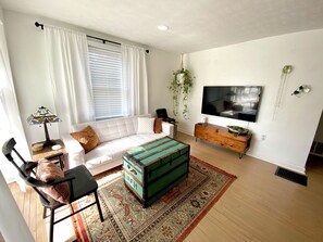 A modern living room with a white sofa, a colorful ottoman, a TV, and a wooden cabinet. - Peaceful + Cozy 2BR Oasis (Dayton)