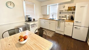 A compact kitchen with white cabinets, a wooden table with a bowl of apples, a coffee maker, and a white refrigerator. - Peaceful + Cozy 2BR Oasis (Dayton)