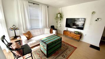 A modern living room with a white sofa, a colorful ottoman, a flat-screen TV, and a wooden cabinet.