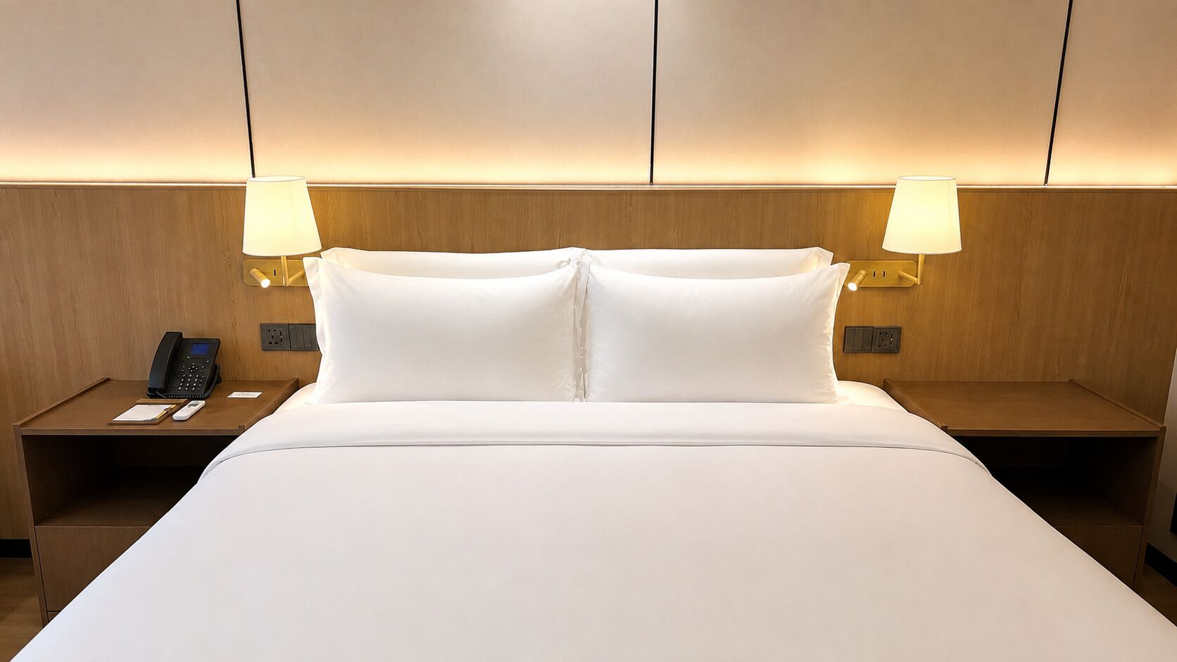 A hotel room with a large bed, two bedside tables, a telephone, and two lamps.