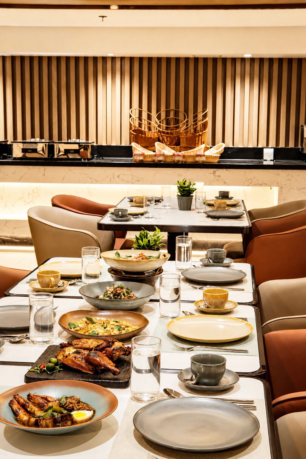 Un comedor con una mesa dispuesta para una comida, sillas y una zona de cocina al fondo.