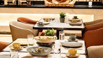 Un comedor con una mesa dispuesta para una comida, sillas y una zona de cocina al fondo.