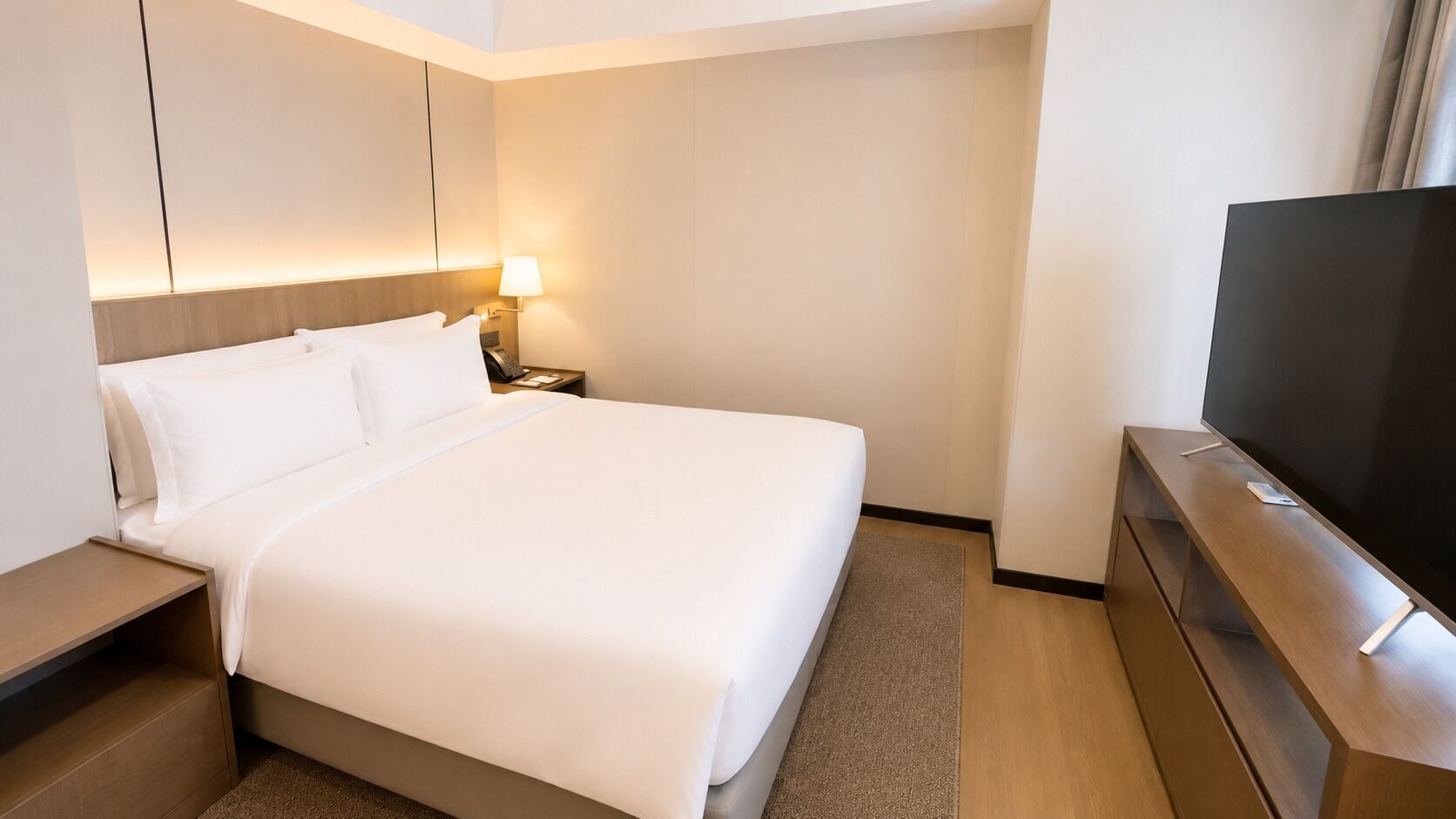 A hotel room with a bed, bedside table, lamp, and a television.