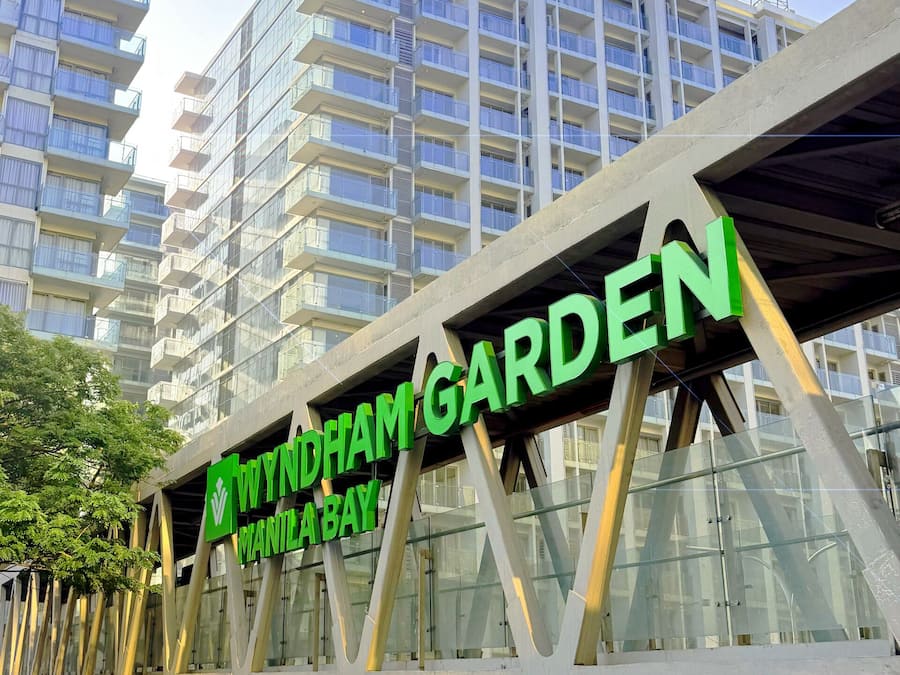 Un edificio moderno con un letrero que dice 'WYNDHAM GARDEN MANILA BAY' y un letrero de altura libre de 4,89m.