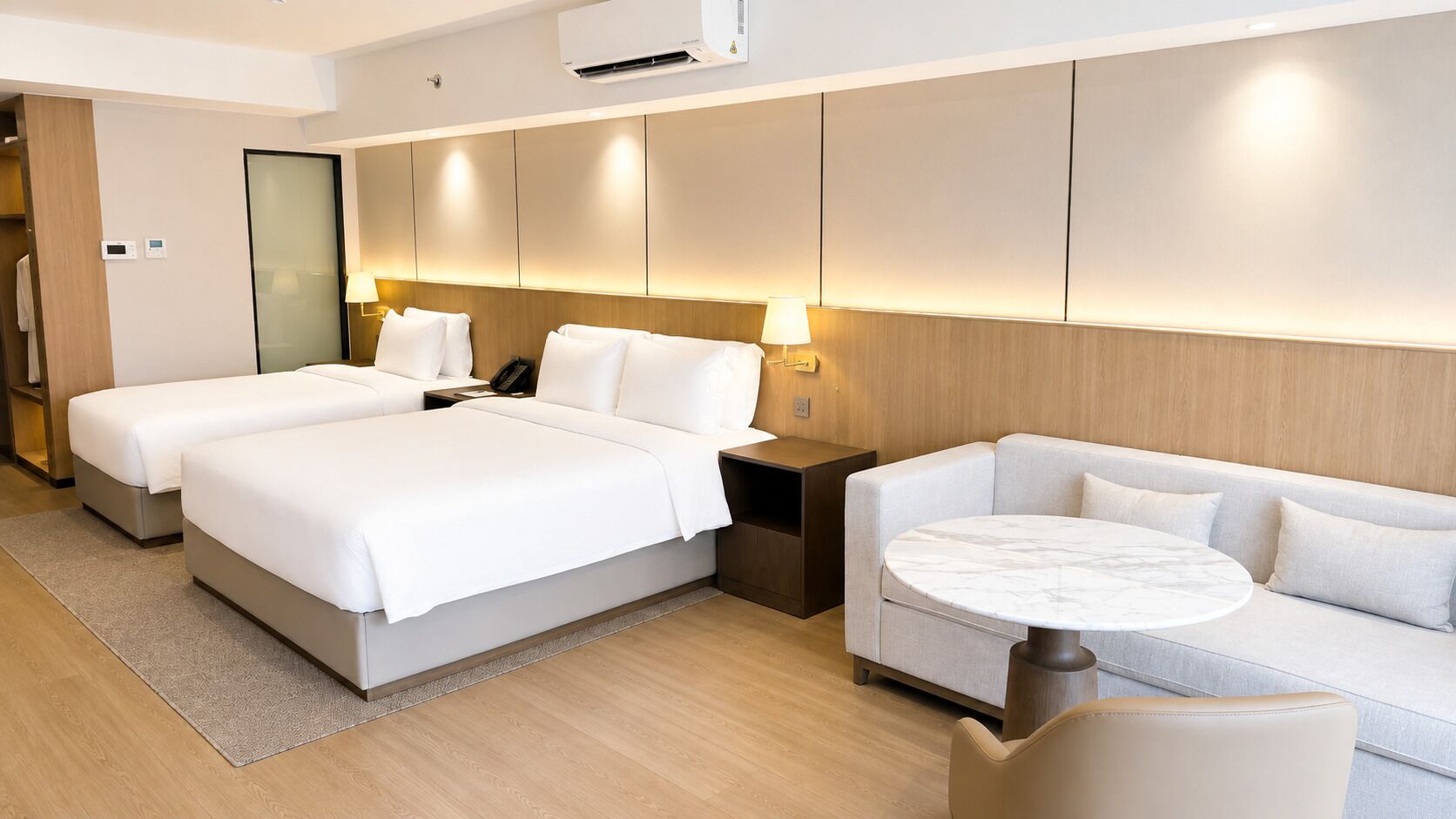 A hotel room with two beds, a sofa, a round table, and a mirror.