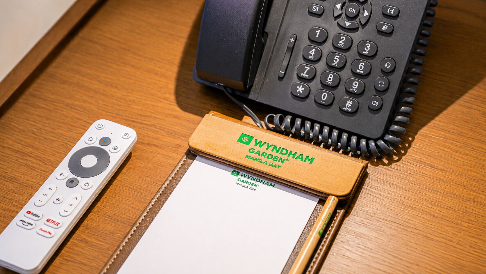 Un control remoto, una libreta y un teléfono sobre una superficie de madera.