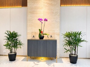 A reception desk with a grey tablecloth, two potted plants, and a vase with orchids. - Wyndham Garden Manila Bay (Parañaque)