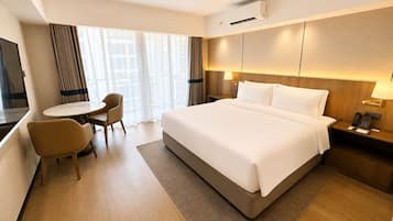 Una habitación de hotel con una cama grande, un escritorio, una silla y un ventanal con cortinas.