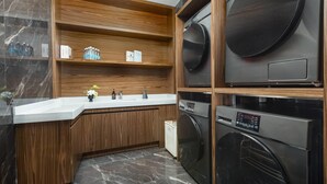 Une cuisine moderne dotée d’un plan de travail en marbre, de meubles en bois et d’appareils électroménagers intégrés, notamment un lave-linge et un sèche-linge.