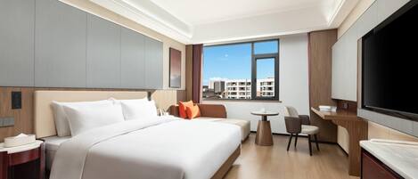 A hotel room with a large bed, a desk, a TV, and a view of buildings outside the window.
