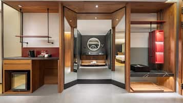 Una habitación de hotel moderna con un espejo central, un tocador con un espejo redondo, una cama y un armario rojo.
