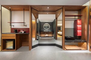 Una habitación de hotel moderna con un espejo central, un tocador con un espejo redondo, una cama y un armario rojo.