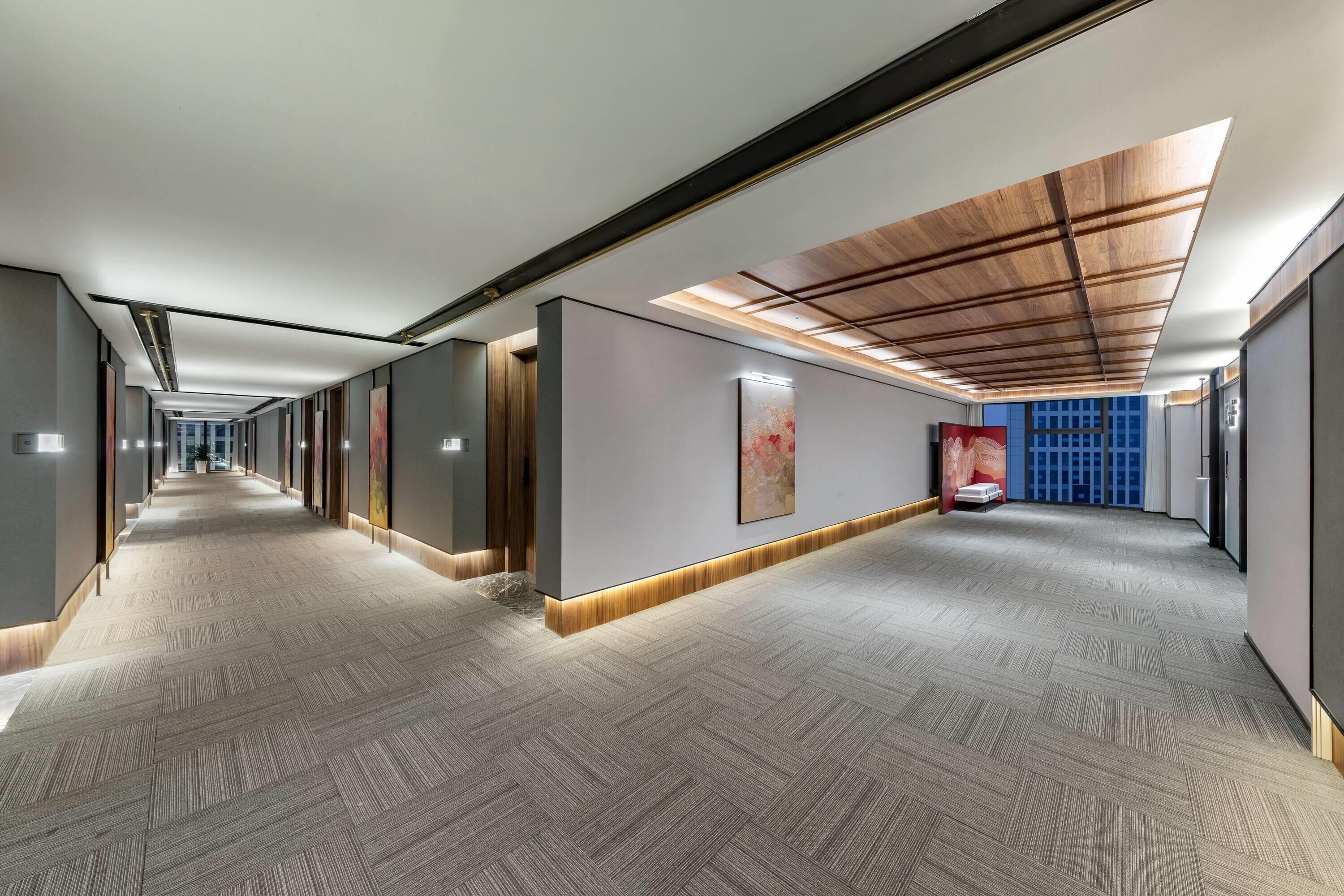 Een moderne hotelgang met een patroon vloerkleed, inbouwverlichting en een houten plafond.