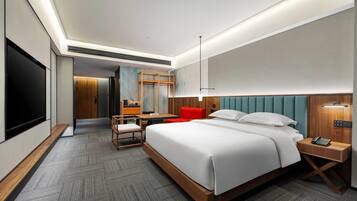 Een moderne hotelkamer met een groot bed, een bureau, een stoel, een televisie en een rode fauteuil.