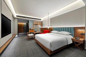 A modern hotel room with a large bed, a desk, a chair, a TV, and a red accent chair. - Hawthorn By Wyndham Yueyang Railway East Station (Yueyang)