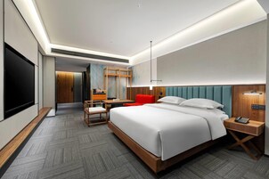 A modern hotel room with a large bed, a desk, a chair, a TV, and a red accent chair.