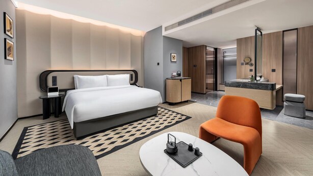 Una camera d'albergo moderna con un letto, una scrivania, una sedia, un bagno e un'area ristorazione.