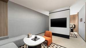 A modern hotel room with a flat-screen TV mounted on the wall, a small round table with a chair, a sofa, and a patterned rug. - Days Hotel By Wyndham Changsha Xingsha (Changsha)