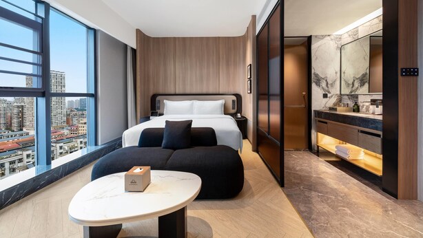 A modern hotel room with a large bed, a sitting area, a vanity, and a view of the city. - Days Hotel By Wyndham Changsha Xingsha (Changsha)
