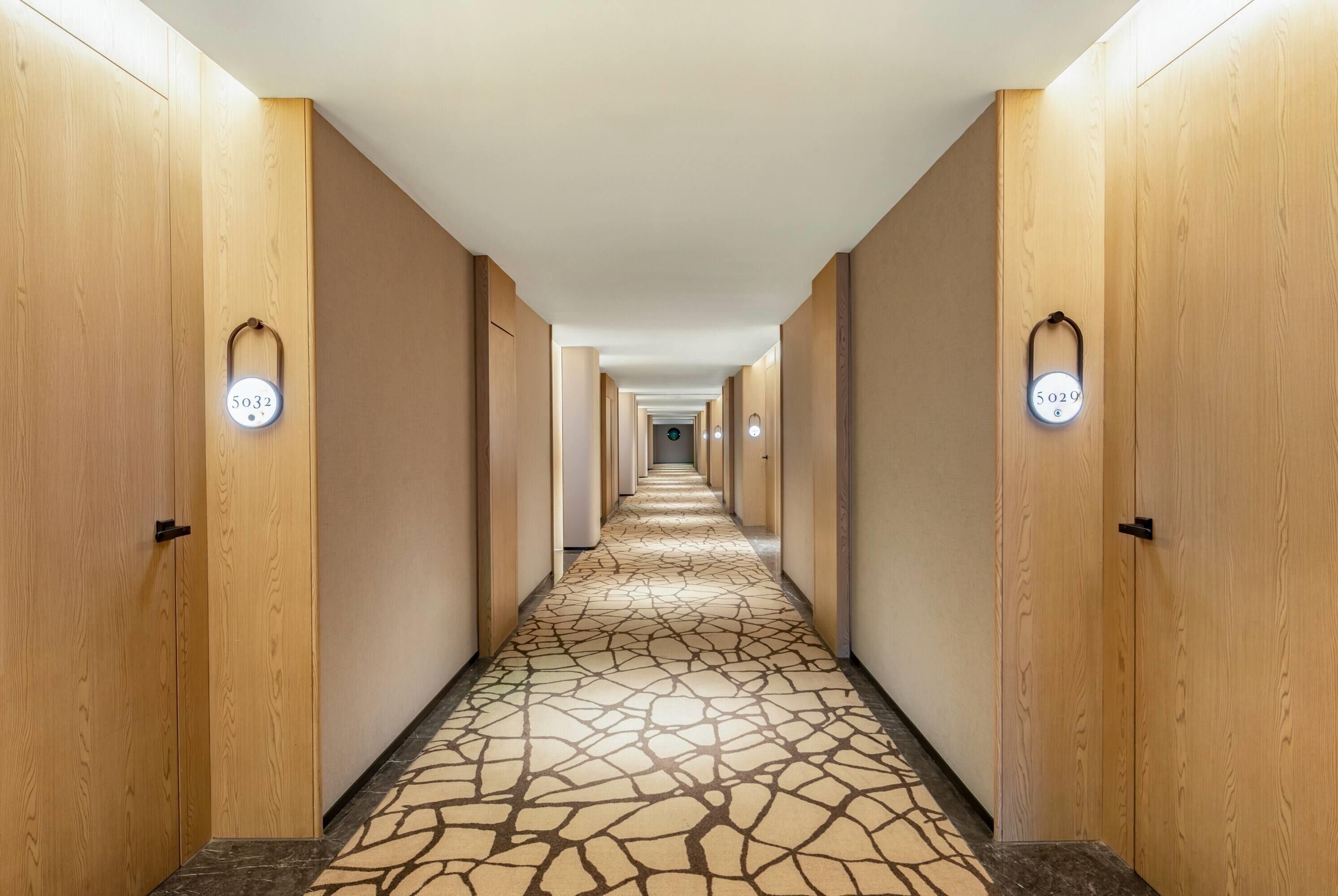 Un corridoio d'albergo con porte in legno, serrature numerate e pavimento decorato.