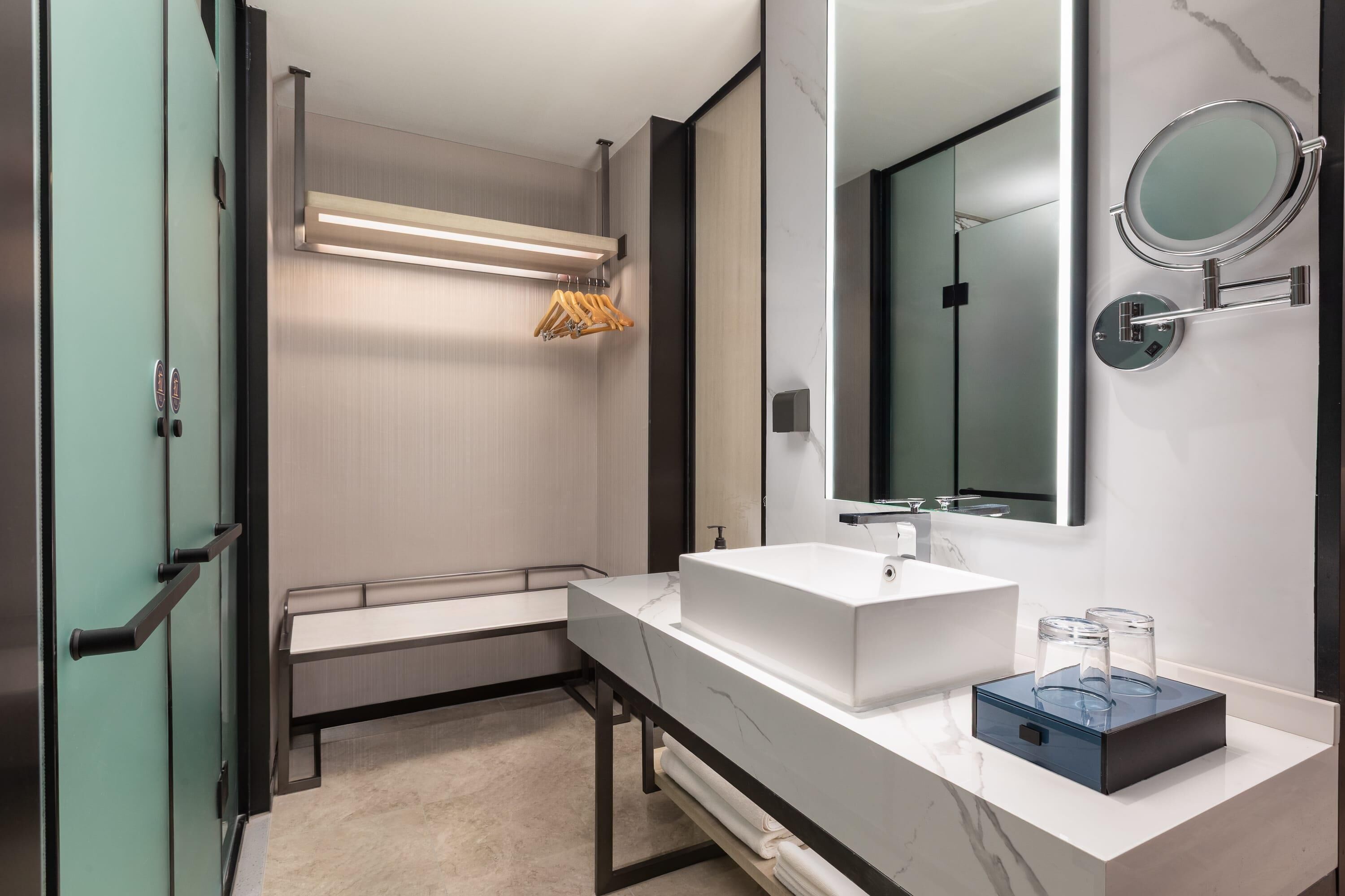 A modern bathroom with a large mirror, a white sink, and a towel rack.