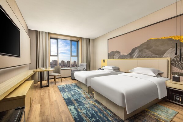 Habitación de hotel con dos camas, un escritorio, una silla, un televisor y un amplio ventanal con vistas a la ciudad.
