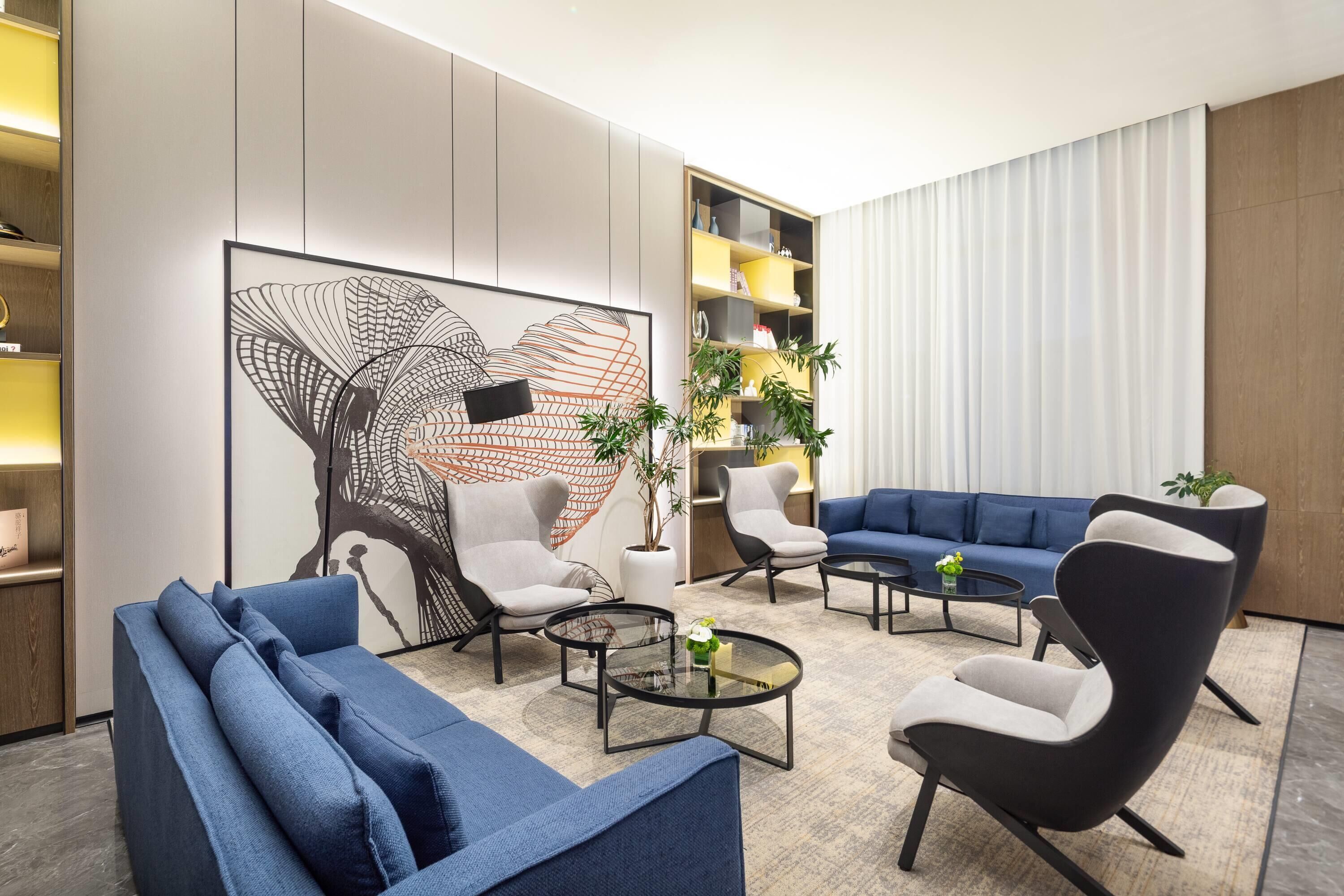 Een moderne woonkamer met een blauwe bank, fauteuils, een salontafel en een groot abstract schilderij.