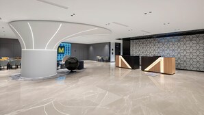 Een moderne lobby met een centraal receptiegedeelte, een zithoek en een wand met een geometrisch patroon.