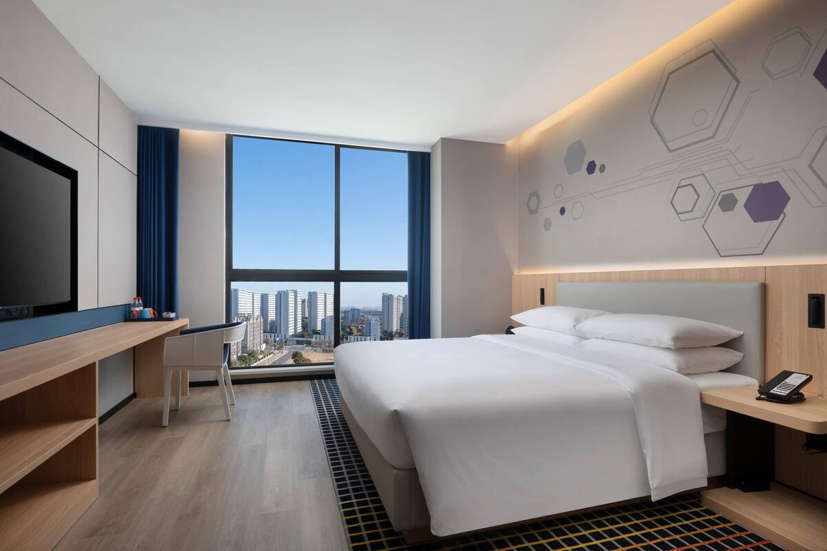 Ein modernes Hotelzimmer mit einem großen Bett, einem Schreibtisch und Blick auf die Stadt.