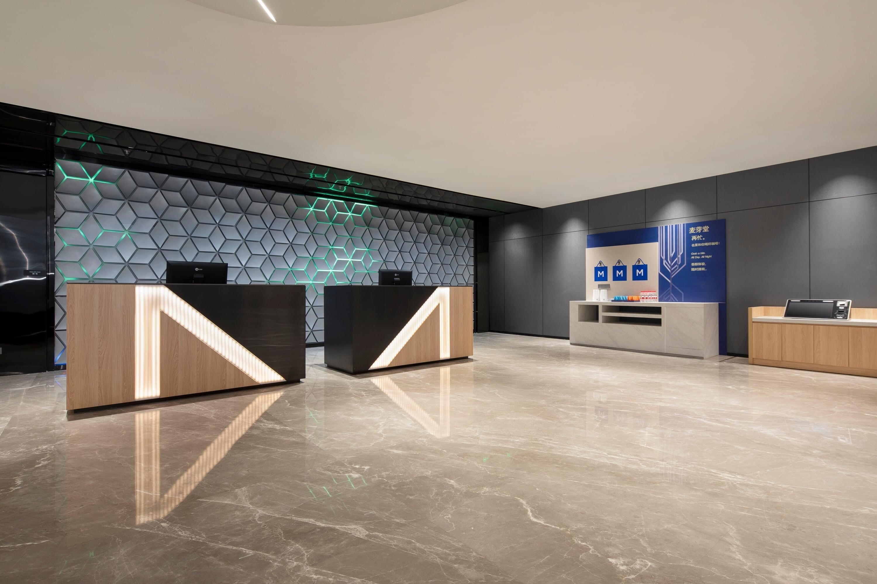 A modern reception area with two reception desks, a geometric patterned wall, and a blue informational sign.