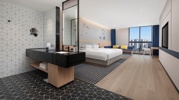 Een moderne hotelkamer met een groot bed, een badkamer met een zwart aanrecht, een grote spiegel en uitzicht op de stad.
