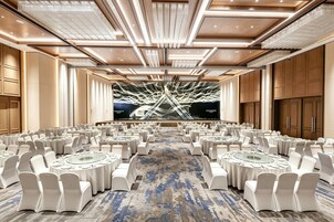 A large conference room with round tables, white chairs, and a large screen at the front.