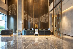 Una zona de recepción moderna con suelo de mármol, un mostrador y una instalación de luces decorativas en el techo.