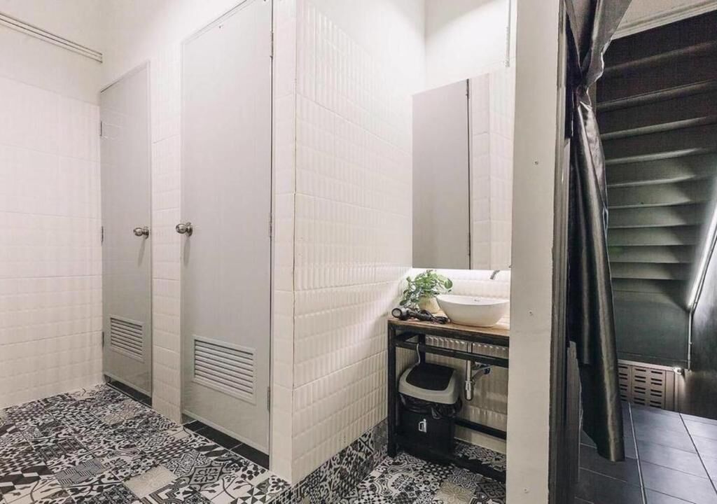 Casa de banho com paredes revestidas a azulejos brancos, chão com padrão preto e branco, lavatório com espelho e uma porta.