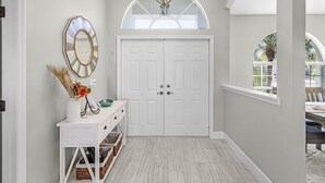 Un couloir avec une porte blanche, une console sur laquelle sont posés un vase et des objets décoratifs, un miroir et un lustre.