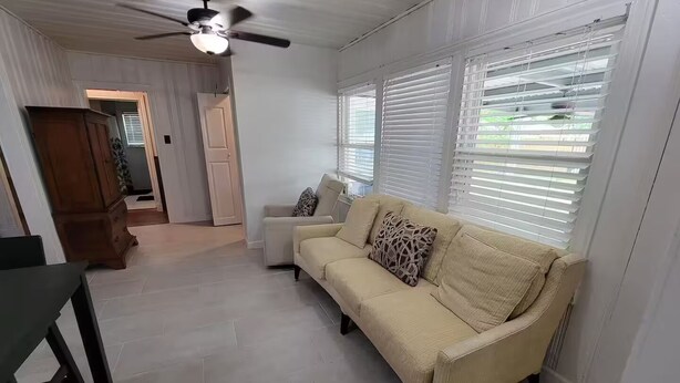 Una sala de estar con un sofá color beige, un aparador de madera y un ventilador de techo.