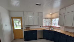 Una cocina con armarios blancos, encimera de madera y lavavajillas integrado.