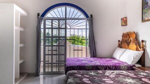 Ein Schlafzimmer mit Bett, Holz-Kopfteil, Balkontür und Blick ins Grüne.