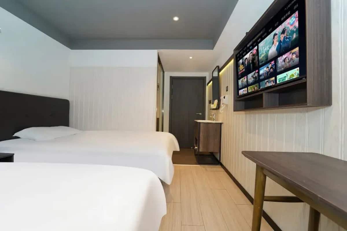 A hotel room with two beds, a TV mounted on the wall displaying movie options, and a small table.