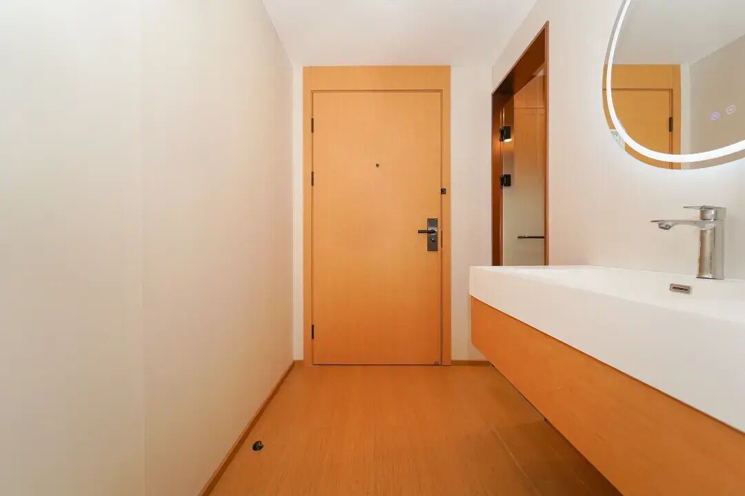 A modern bathroom with a wooden door, a white sink, and a mirror with a lighted frame.