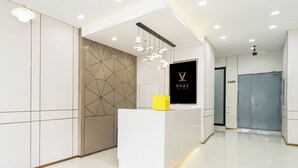 A modern hotel reception area with a geometric patterned wall, a reception desk with a yellow folder, and a grey door leading to a shower area. - Jinglai Hotel ShanghaiWujiaochang Branch (Shanghai)