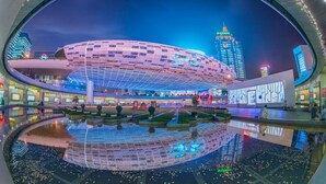 A modern building with a unique curved design, surrounded by a reflective water feature and illuminated by ambient lighting. - Jinglai Hotel ShanghaiWujiaochang Branch (Shanghai)