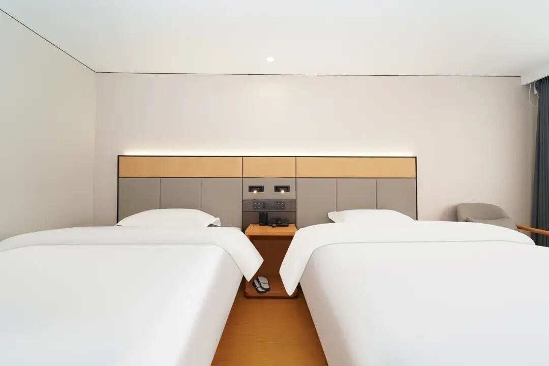 A hotel room with two beds, a nightstand with a lamp, and a small table.