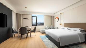 Habitación de hotel moderna con una cama grande, un escritorio con dos sillas, un televisor y ventana con vista a las montañas.