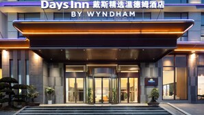 Entrada de un hotel con diseño moderno, destacando una fachada de vidrio y un letrero que indica que es un Days Inn by Wyndham.