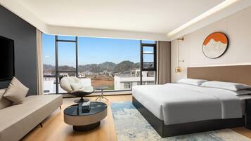 Una habitación de hotel moderna con una cama grande, un sofá, una pequeña mesa redonda y un televisor.