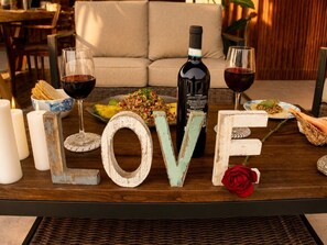 A table with a bottle of wine, glasses, a plate of food, candles, and decorative letters spelling 'LOVE' with a rose. - Top Floor Suite +Pool +Private Path to Shore, A/C. Accessible step-less layout (San Pedro Pochutla)